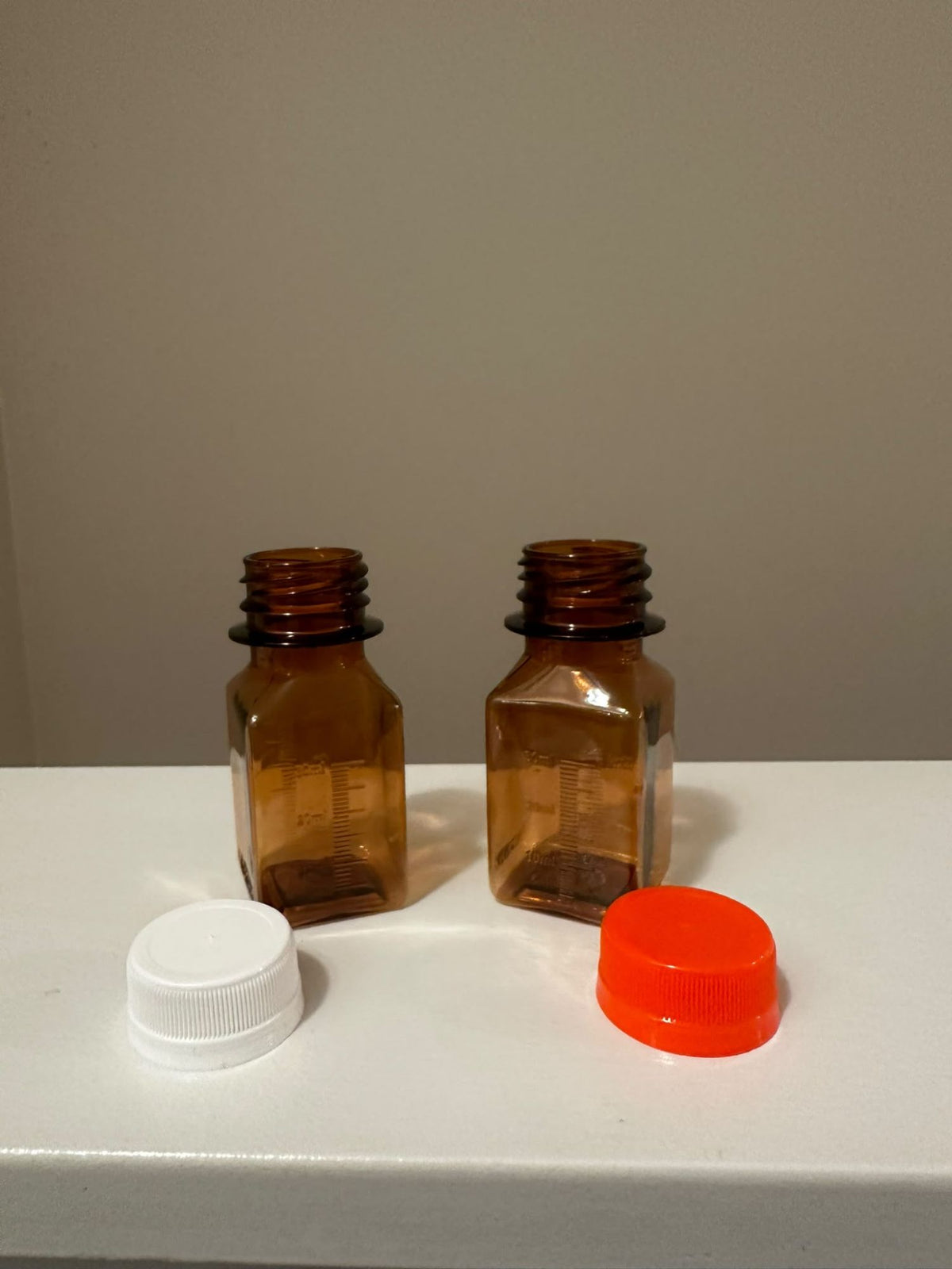 Two amber graduated methadone bottles shown with white and orange push and turn caps